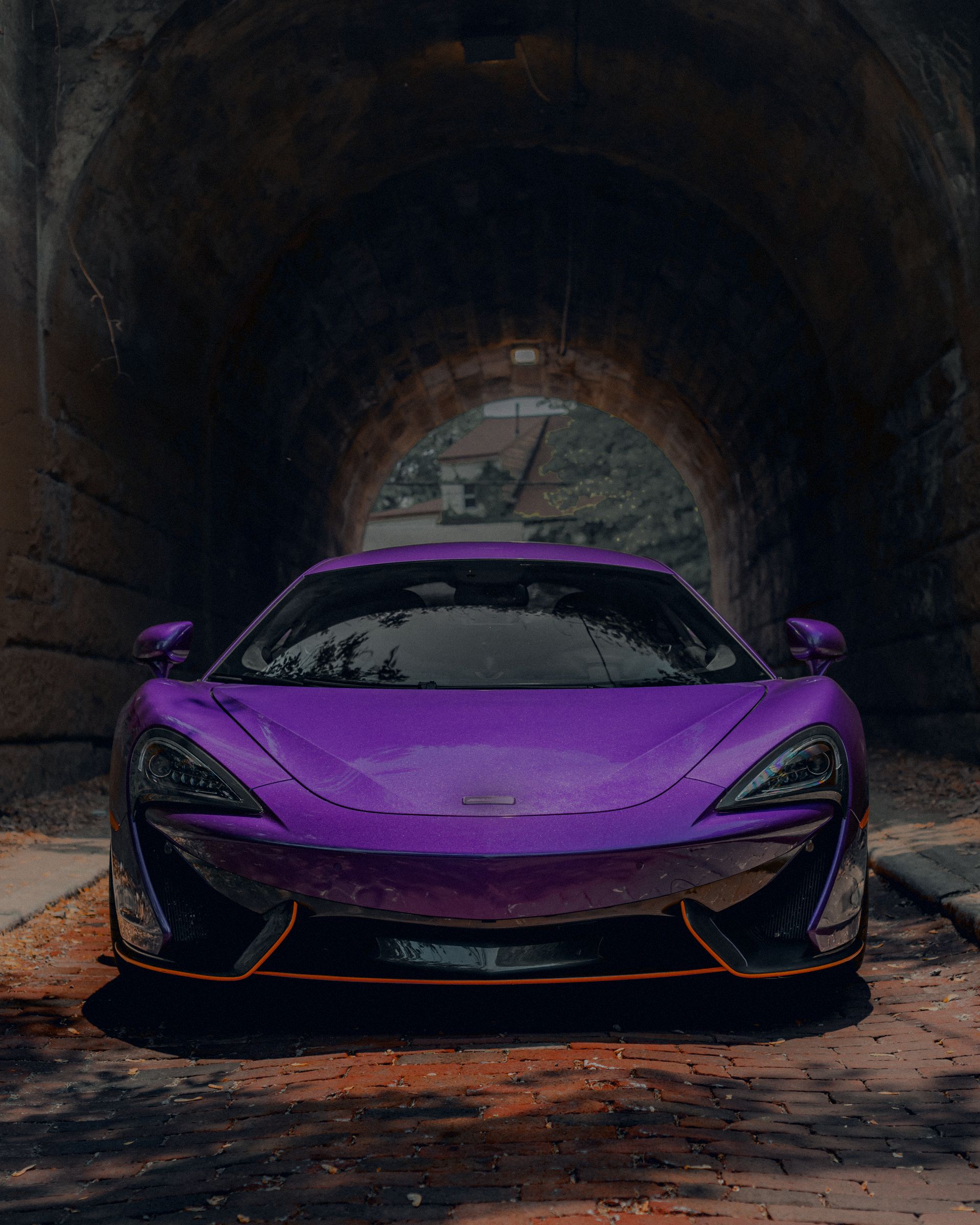 A purple mid-engine coupe parked head-on inside a brick tunnel arch