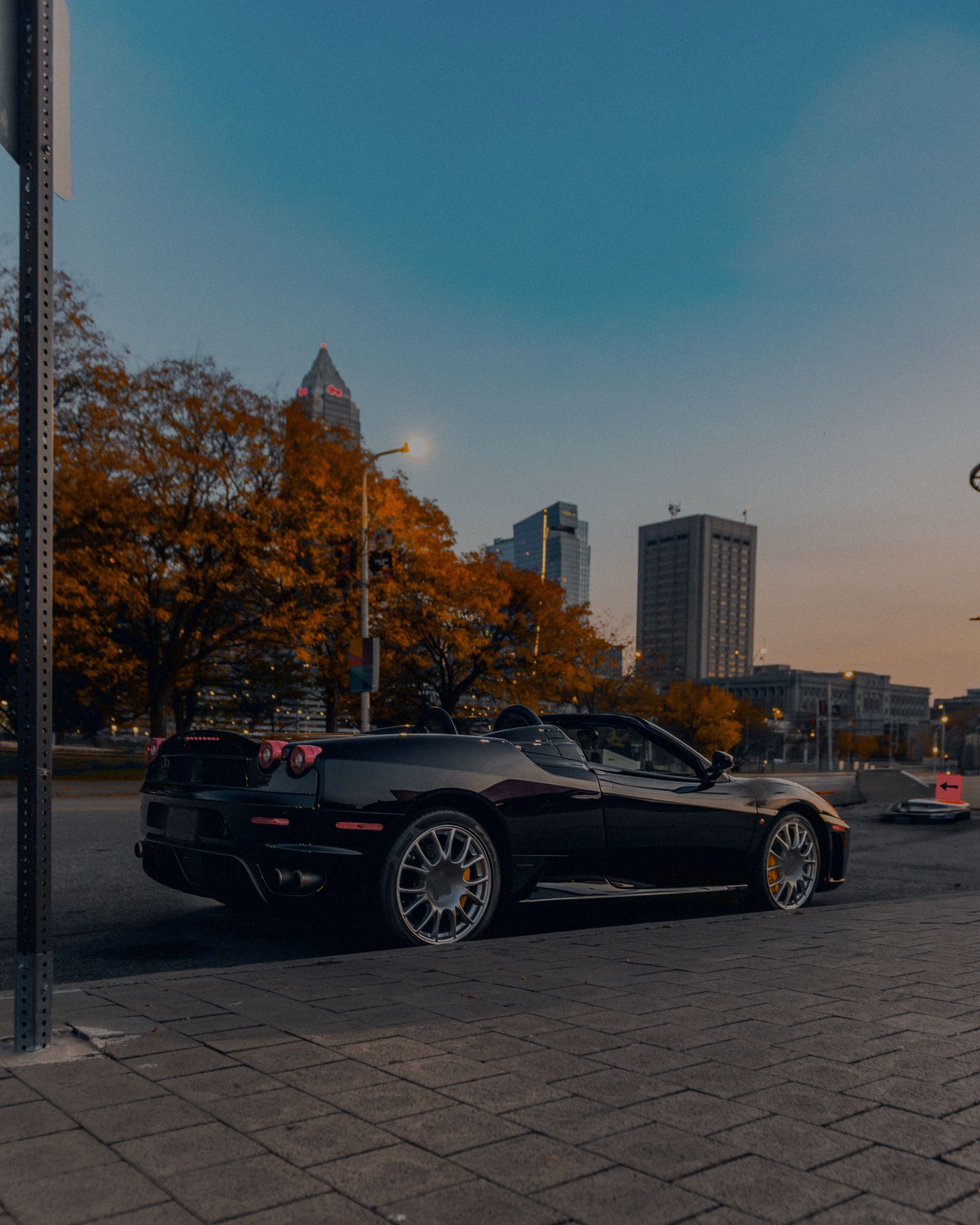 Black convertible parked at dusk under orange fall trees and city towers